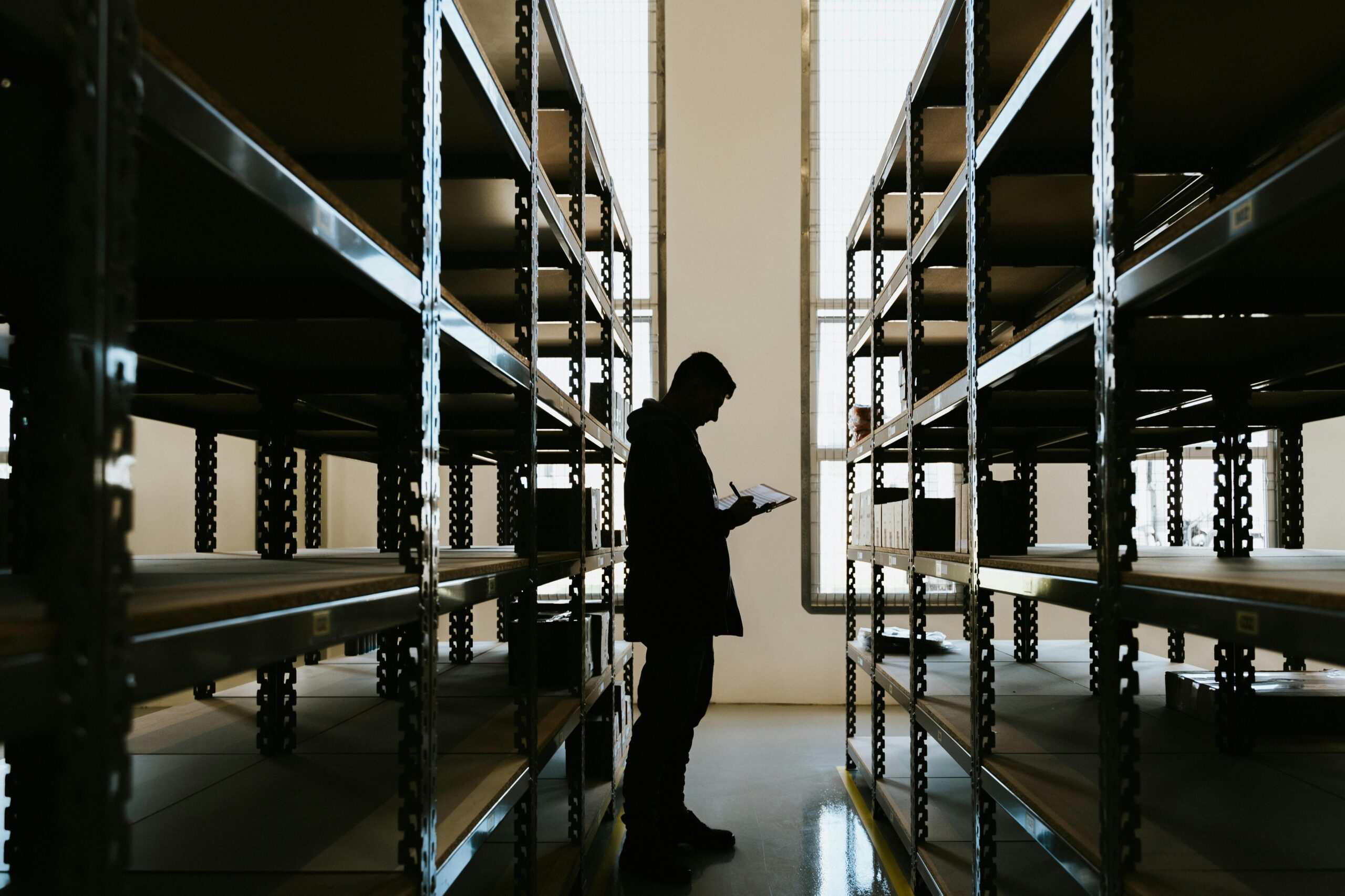 Silhouette of a person checking inventory in an empty warehouse with racks.